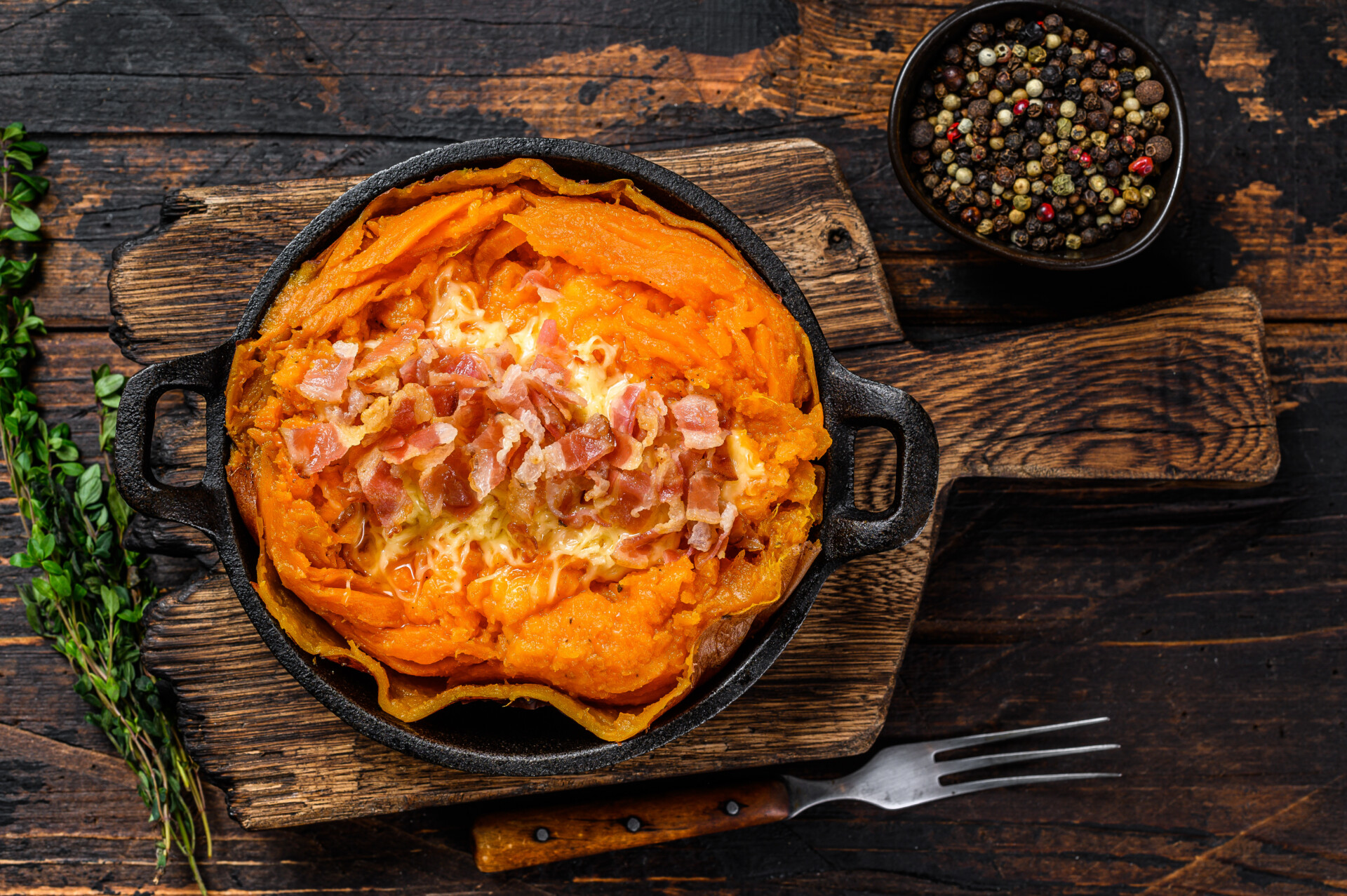 Baked in skin sweet potato batata stuffed with cheese and bacon. Dark Wooden background. Top view